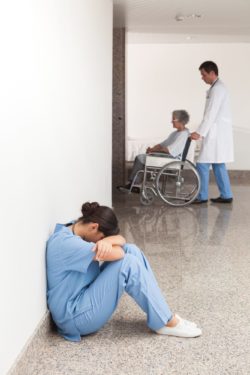 Nurse sitting in hallway with head in arms and doctor pushing a wheelchair regarding the Altamont Care Community class action lawsuit filed after residents die of COVID-19