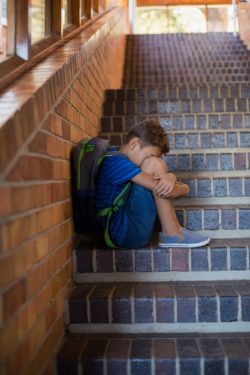 Sad child with backback sitting on stairs regarding the teacher sexual abuse class action lawsuit allowed to move forward