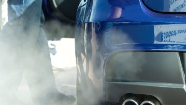 Person standing next to car emitting exhaust regarding the Bosch emissions cheating device class action settlement
