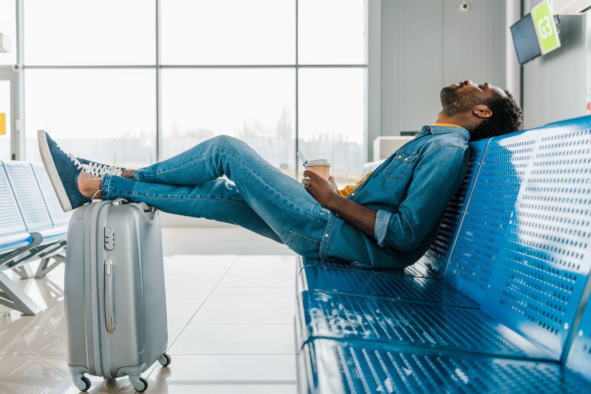 man lying on airport bench waiting for cancelled flight amid COVID-19 cancellation vouchers