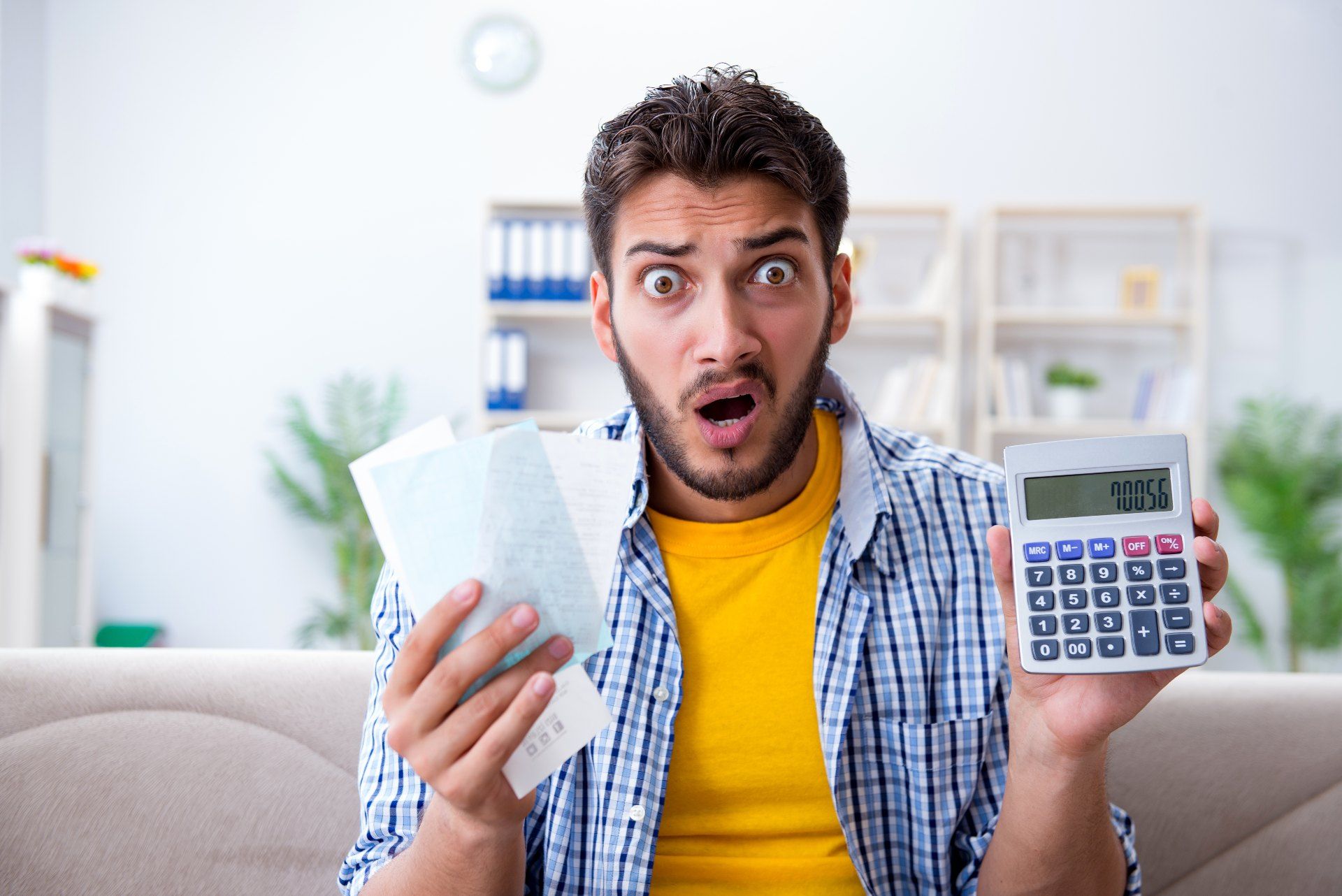 A shocked man holds receipts and a calculator - overdraft fees