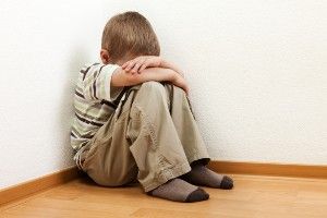 Boy sits in a corner with his legs pulled up to his chest and his head lying on his crossed arms - sexual abuse