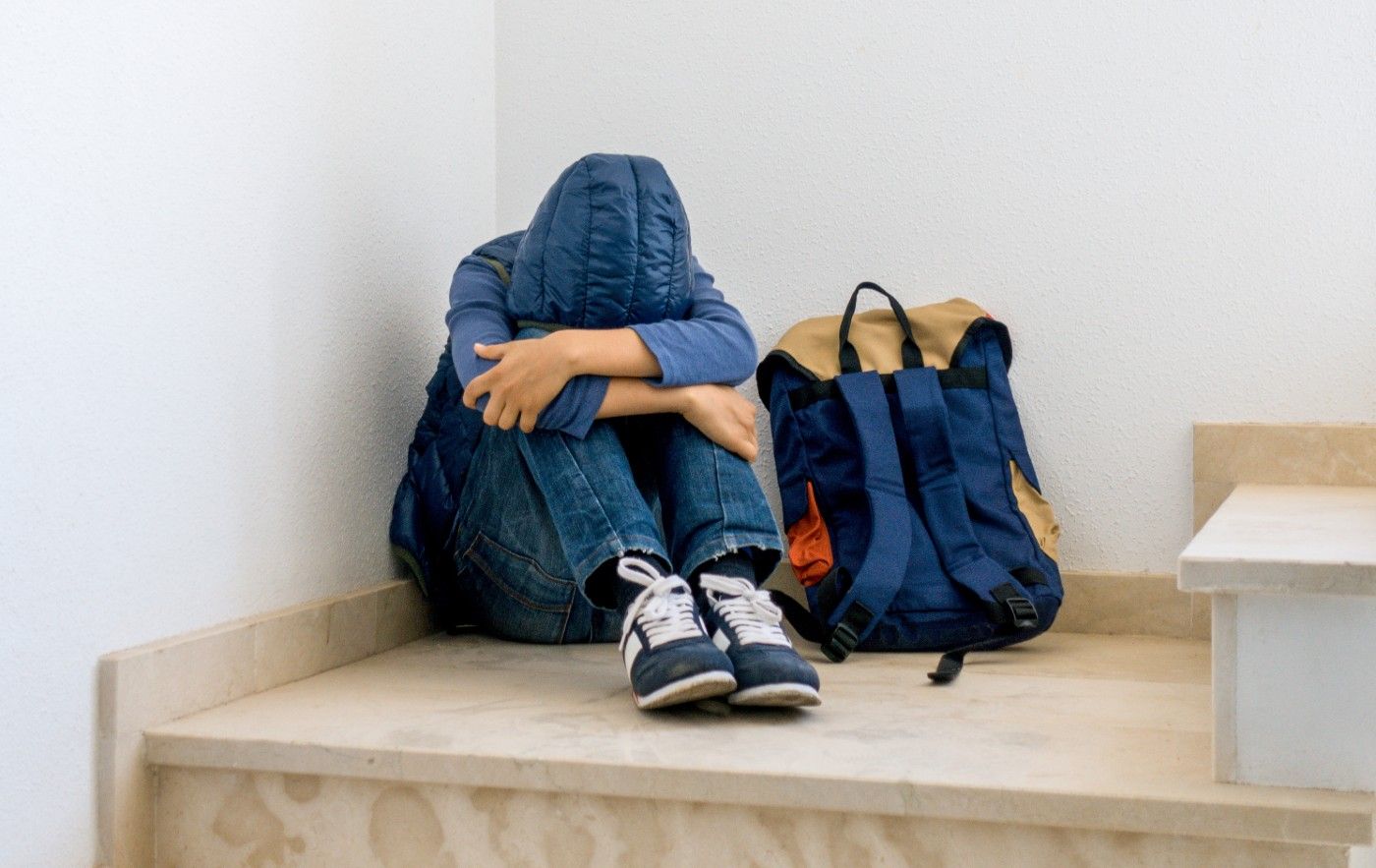 Scared boy in hooded coat sits on stair landing with backpack - sexual abuse