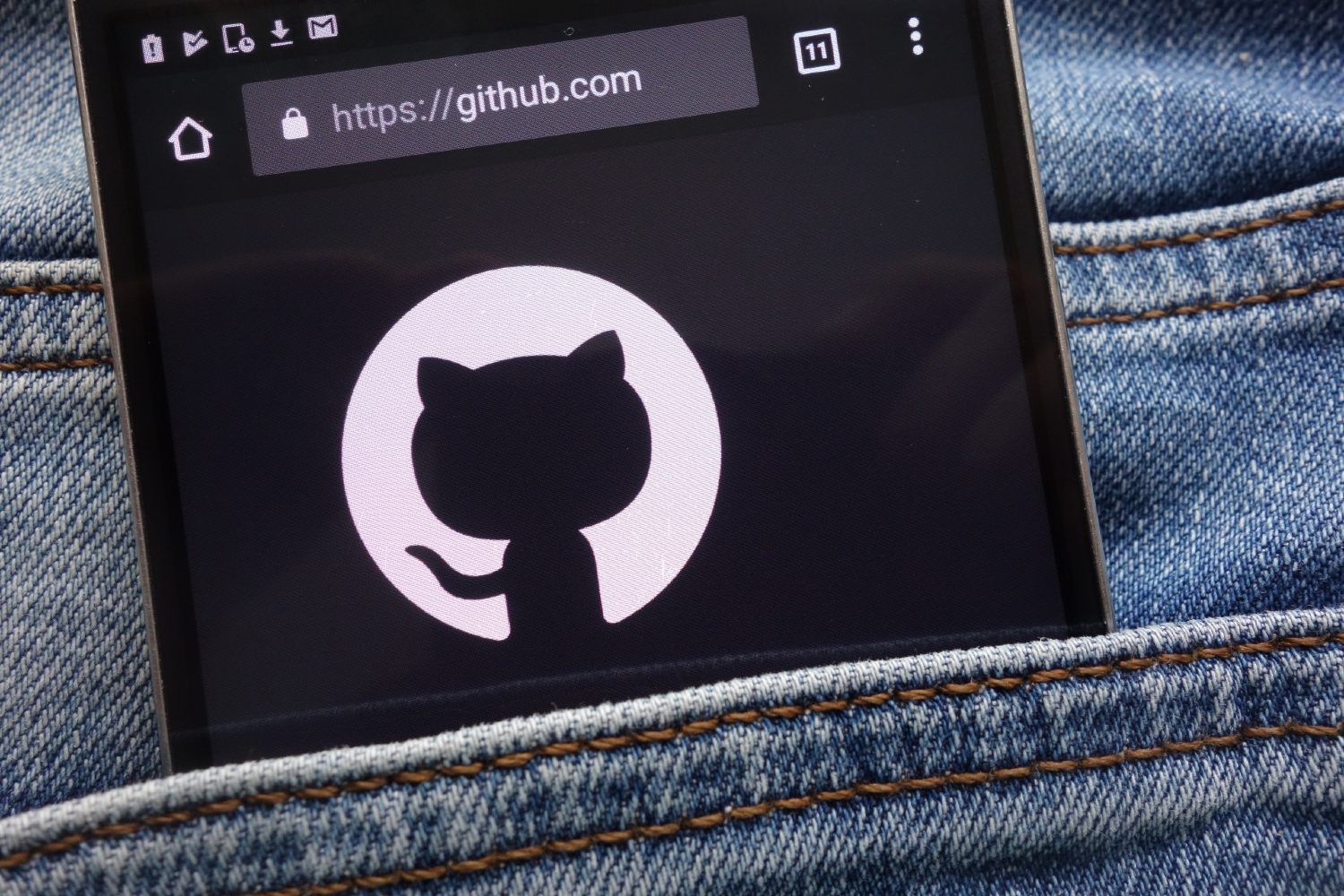 A smartphone with GitHub on the screen sticks out of a pocket on bluejeans