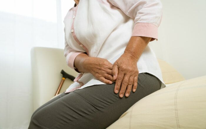 A woman grabs her hip in pain as she sits on the edge of a bed - DePuy ASR lawsuit - DePuy class action settlement