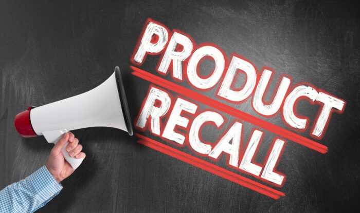 hand holding megaphone or bullhorn against blackboard with text PRODUCT RECALL