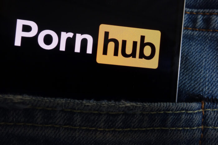 Pornhub logo displayed on smartphone hidden in jeans pocket.