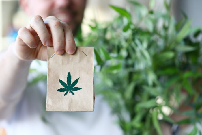 Male hand hold paper packet with marijuana symbol closeup background.
