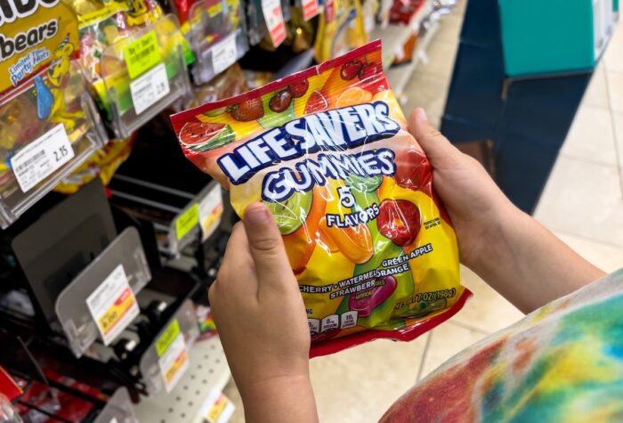 Child's hand holding a bag of Lifesavers brand gummies candy in a supermarket aisle.