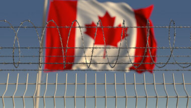 A Canada flag waving in the wind behind a prison fence.