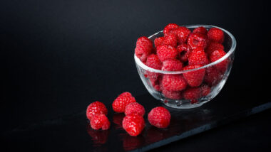 Fresh raspberries in a ceramic bowl isolated on a black background.