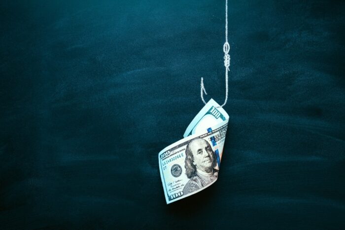 A U.S. $100 bill on a fishing hook against a dark blue background. sweepstakes scam concept, representing the Next-Gen FTC refunds.