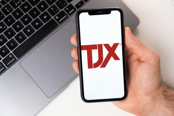 Close up of a males hand holding a smartphone with the TJX logo displayed.
