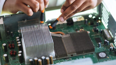 Close up of a persons hands using tools to fix the motherboard of a computer.