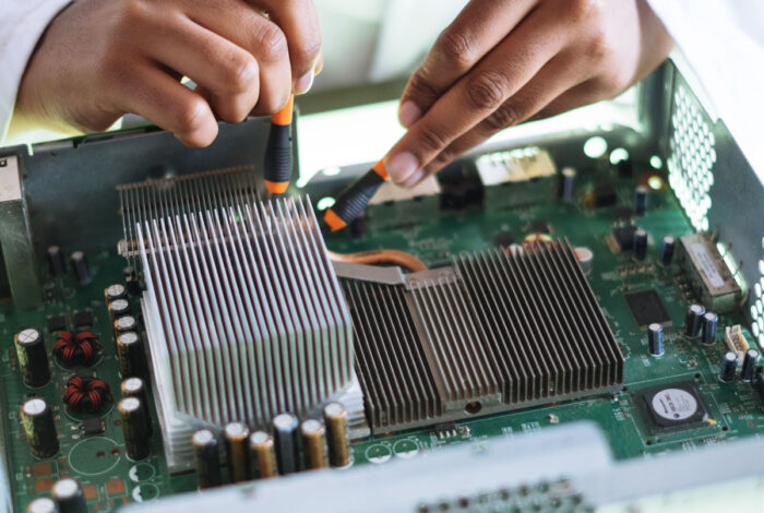 Close up of a persons hands using tools to fix the motherboard of a computer.