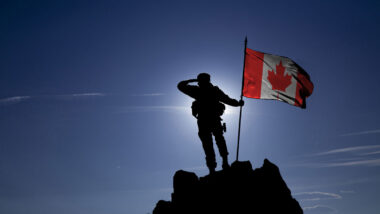 Soldier on top of the mountain with the Canadian flag.