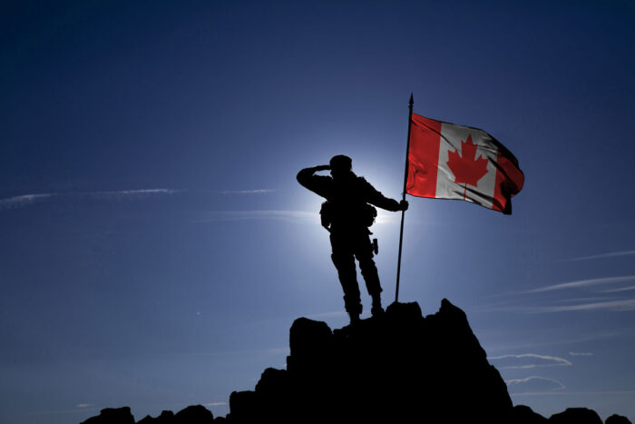 Soldier on top of the mountain with the Canadian flag.