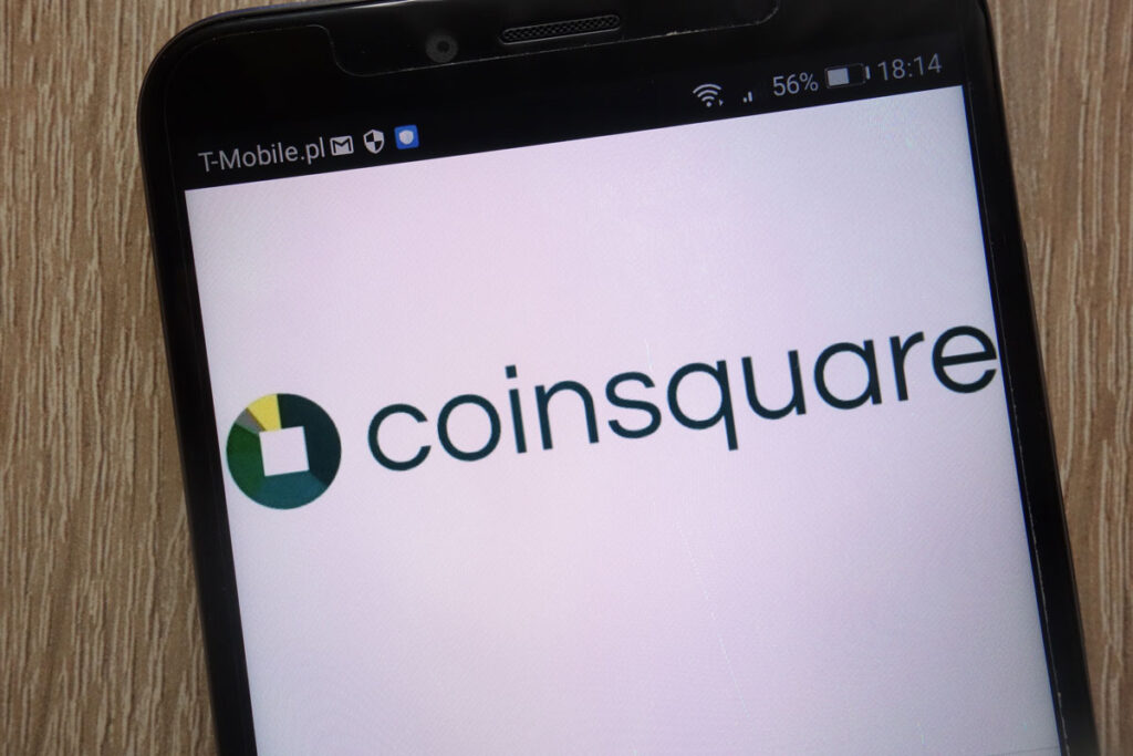 Coinsquare logo displayed on a modern smartphone against a wooden background.