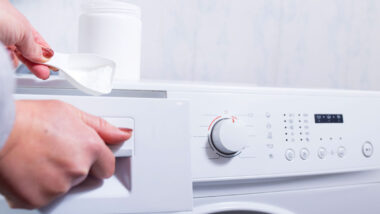 Close up of a woman's hand putting laundry detergent in a washing machine.