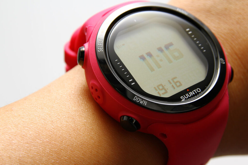 Close up of a red Suunto diving computer on a womans wrist, representing the Suunto defective dive computer settlement.