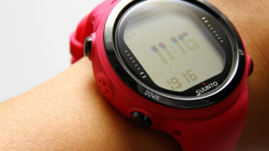 Close up of a red Suunto diving computer on a womans wrist, representing the Suunto defective dive computer settlement.