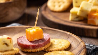 Closeup of sliced salami, cheese cubes and crackers on a wooden plate.