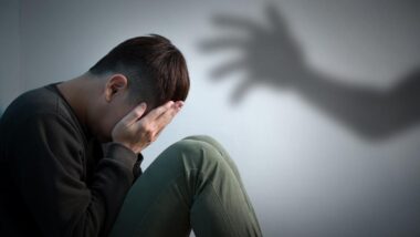 A young male crying into his hands with a shadow of a hand reaching out towards him, representing the Newfoundland sexual abuse settlement.