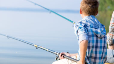 Boy in blue shirt sit on a pier with a fishing rod by the sea