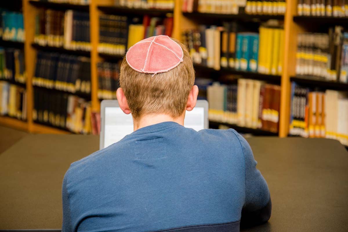 Back view of a male wearing a yarmulke studying on his laptop, representing the anti-semitic universities class action.