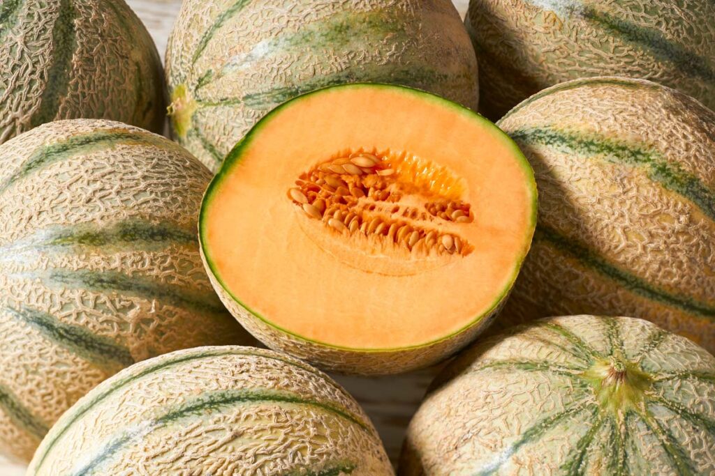 A slice cantaloupe melon atop a group of cantaloupe melons, representing the cantaloupe recall.